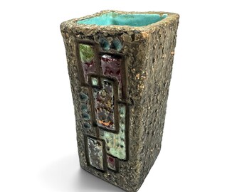 May include: A rectangular ceramic vase with a rough, dark brown textured exterior. The front face features inlaid geometric panels in shades of green, burgundy, and blue. The interior of the vase is finished in a smooth, bright turquoise glaze.