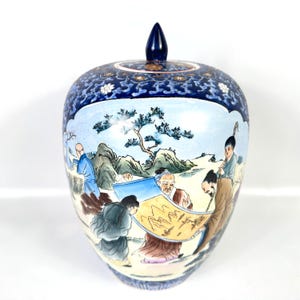 Puede incluir: Un tarro de jengibre de cer&aacute;mica con tapa que presenta una secci&oacute;n superior azul oscuro con patrones florales blancos. El cuerpo muestra una escena pintada a mano de figuras en un paisaje con monta&ntilde;as, &aacute;rboles y un pergamino, en tonos azules, marrones y verdes.