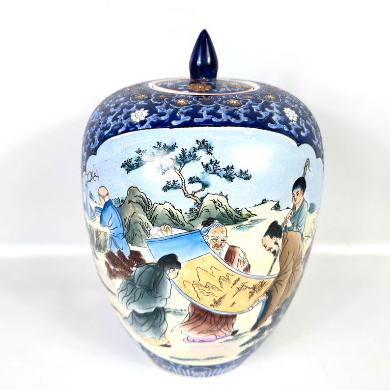 Puede incluir: Un tarro de jengibre de cer&aacute;mica con tapa que presenta una secci&oacute;n superior azul oscuro con patrones florales blancos. El cuerpo muestra una escena pintada a mano de figuras en un paisaje con monta&ntilde;as, &aacute;rboles y un pergamino, en tonos azules, marrones y verdes.