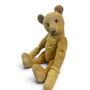 May include: A vintage-style teddy bear crafted from golden-brown textured fabric. The bear features dark, round eyes, a stitched black nose and mouth, and prominent ears. It wears ribbed, light-colored knitted cuffs on its arms and legs.