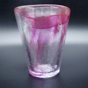 Puede incluir: Un vaso de vidrio transparente con forma acampanada y superficie texturizada. El vidrio est&aacute; adornado con vetas y una banda de color magenta intenso. El dise&ntilde;o es simple y elegante, adecuado para diversas bebidas.