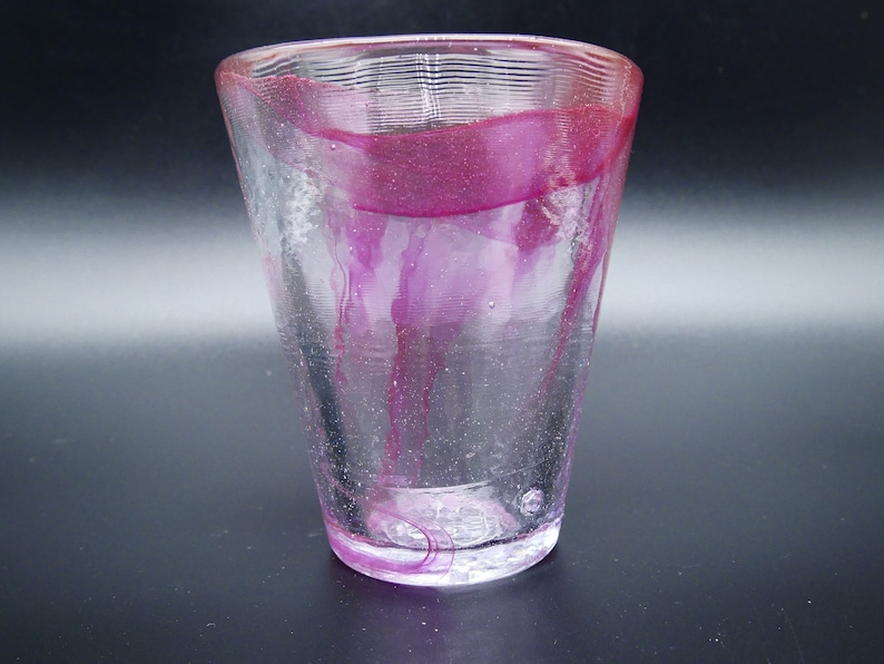 Puede incluir: Un vaso de vidrio transparente con forma acampanada y superficie texturizada. El vidrio est&aacute; adornado con vetas y una banda de color magenta intenso. El dise&ntilde;o es simple y elegante, adecuado para diversas bebidas.