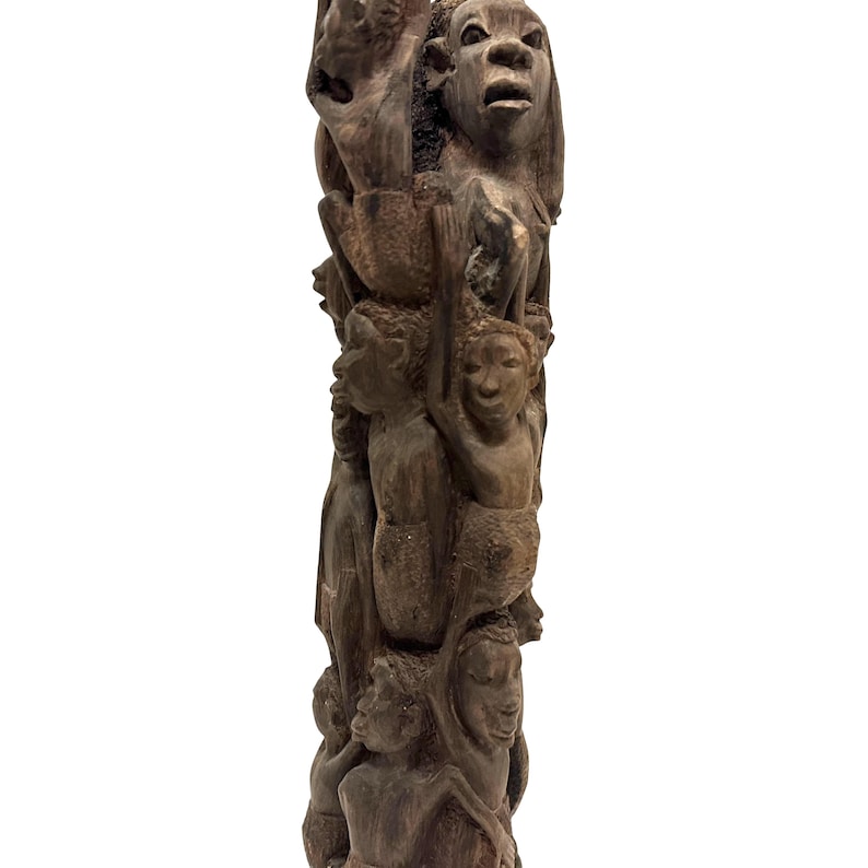 May include: A tall, dark brown wooden sculpture featuring a vertical arrangement of multiple human figures carved in relief. The figures are stacked and intertwined, displaying various facial expressions and postures, with a textured, matte finish.