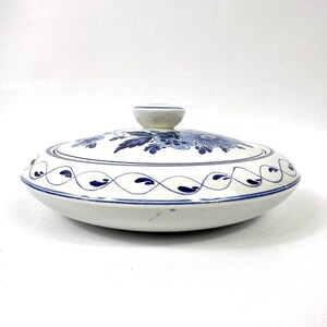 May include: An oval white ceramic serving dish with a lid. The lid and the dish are decorated with blue floral patterns and a blue border. The lid has a small, round handle. The dish is suitable for serving food.