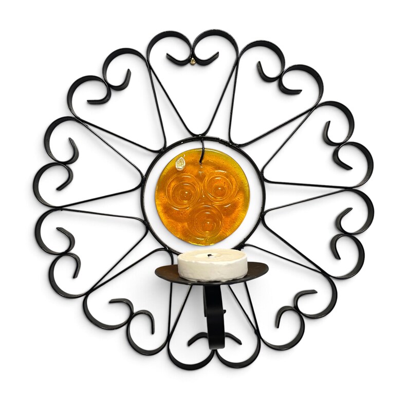 Peut inclure: Une applique murale en m&eacute;tal noir dot&eacute;e d'un cadre circulaire avec des volutes d&eacute;coratives et des motifs en forme de c&oelig;ur. Un disque en verre ambr&eacute; avec trois cercles en relief est suspendu au centre, au-dessus d'un petit support &agrave; bougie.