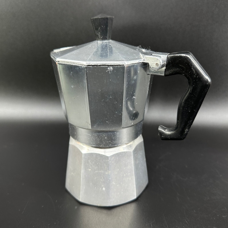 Puede incluir: Una cafetera italiana de aluminio plateado con un mango de pl&aacute;stico negro.