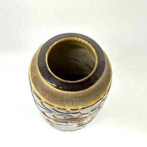 Peut inclure: Un vase en c&eacute;ramique avec un large sommet ouvert et un ext&eacute;rieur textur&eacute;. Le vase pr&eacute;sente un bord marron fonc&eacute; et un corps marron clair avec des motifs floraux sculpt&eacute;s. L'int&eacute;rieur est de couleur beige clair.