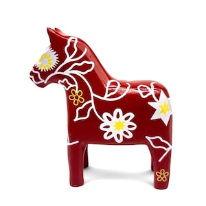 May include: A deep red wooden horse figurine featuring hand-painted white floral patterns and vine motifs. The design includes yellow centers within the white flowers and star-shaped accents, covering the body and head of the horse sculpture.