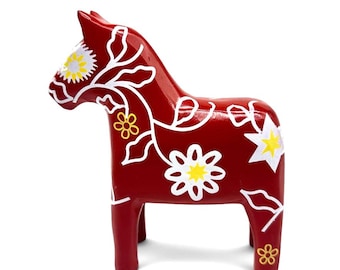 Puede incluir: Una figura de caballo de madera de color rojo oscuro con motivos florales y de enredadera pintados a mano en blanco. El diseño incluye centros amarillos dentro de las flores blancas y detalles en forma de estrella en el cuerpo y la cabeza.