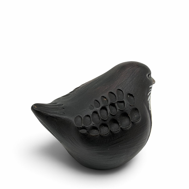 May include: A matte black ceramic bird figurine featuring a rounded body and a pointed tail. The surface is decorated with a series of carved, oval-shaped indentations along the wing area and subtle white painted details near the beak.