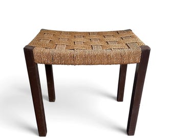 May include: A rectangular stool featuring four dark brown wooden legs and a seat constructed from a woven tan cord pattern. The seat has a slightly curved profile, and the legs are straight, providing a stable base for this piece of furniture.