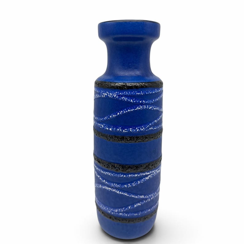 May include: A cylindrical ceramic vase with a matte cobalt blue finish. The body features horizontal bands of textured black glaze interspersed with thin, wavy white lines that wrap around the exterior surface of the vessel.