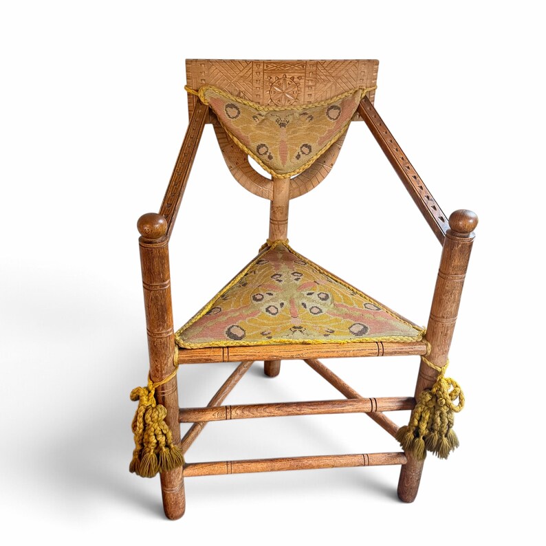 May include: A wooden corner chair featuring a triangular seat and a backrest upholstered in fabric with a moth pattern. The chair has carved details on the frame, yellow braided trim, and decorative yellow tassels hanging from the front legs.