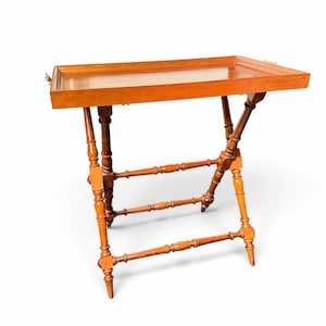 Puede incluir: Una mesa de servicio rectangular de madera con un acabado pulido y liso. La mesa cuenta con una bandeja extra&iacute;ble de bordes elevados y una base plegable formada por cuatro patas torneadas conectadas por travesa&ntilde;os horizontales.