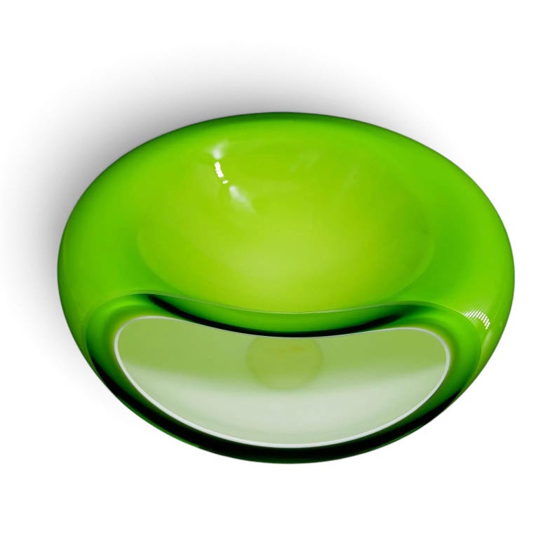 May include: A vibrant lime green glass bowl with a smooth, rounded, and organic shape. The bowl features a wide, circular opening at the top and a secondary, smaller curved opening on the side, creating a hollow, sculptural form with glossy finish.