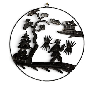May include: A circular black metal wall hanging featuring a silhouette design of a person carrying bundles on a pole across their shoulders, a tree, a small building, and a pagoda structure, all enclosed within a thin black metal circular frame.