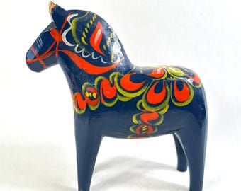 May include: A dark blue wooden horse figurine featuring hand-painted decorative patterns in bright orange and yellow. The horse has a smooth, glossy finish with stylised floral and scroll motifs covering its body, mane, and head in a vibrant colour palette.