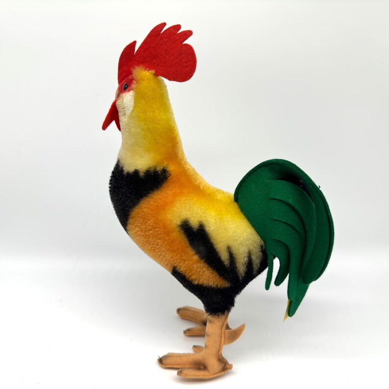 May include: A colorful rooster figurine with a red comb and wattle, yellow and orange body, black accents, and a green tail. The rooster has tan feet and is standing upright. This decorative item is likely a vintage or handmade craft.