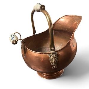 Pu&ograve; includere: Un secchio per carbone in rame con un manico in ottone e una maniglia laterale in ottone. Entrambe le maniglie presentano impugnature in ceramica bianca con motivi floreali blu. I supporti del manico in ottone sono decorati con teste di leone.