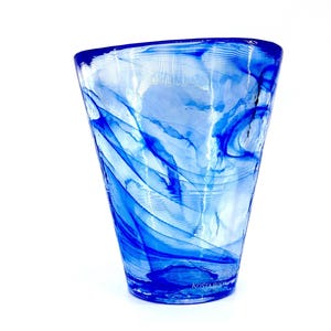 May include: A clear glass vase with a flared shape, featuring swirling blue patterns throughout. The vase has a thick base and a slightly asymmetrical top. The brand name "KOSTA BODA" is visible at the bottom of the vase.