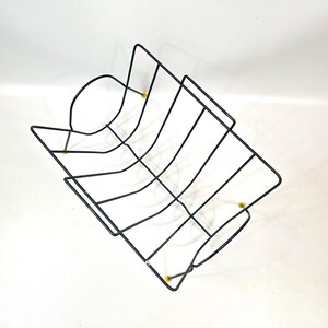 May include: Black wire rack with a rectangular shape and curved sides. The rack has a grid-like design with vertical and horizontal wires. Small yellow accents are visible at the corners. The rack is likely for holding items.