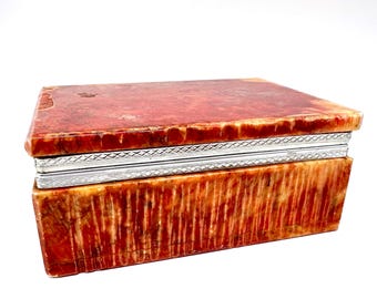 May include: A rectangular jewelry box with a red and cream-colored marbled pattern. The box has a silver-colored metal band around the middle. The box is closed and sits on a white surface.