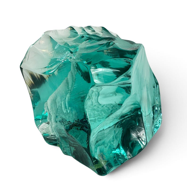 Peut inclure: Une sculpture en verre bleu sarcelle translucide avec une forme irr&eacute;guli&egrave;re et facett&eacute;e. L'int&eacute;rieur contient une figure blanche tridimensionnelle grav&eacute;e d'une ch&egrave;vre de montagne debout sur une surface rocheuse, visible &agrave; travers le verre.