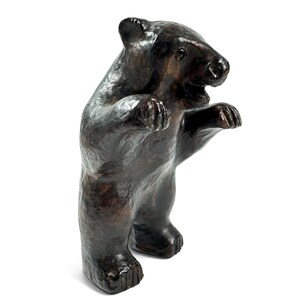 May include: A dark brown bear figurine standing on its hind legs with its front paws raised. The sculpture features a textured, glossy surface with visible brushstrokes and a slightly open mouth, capturing the animal in an upright, alert posture.