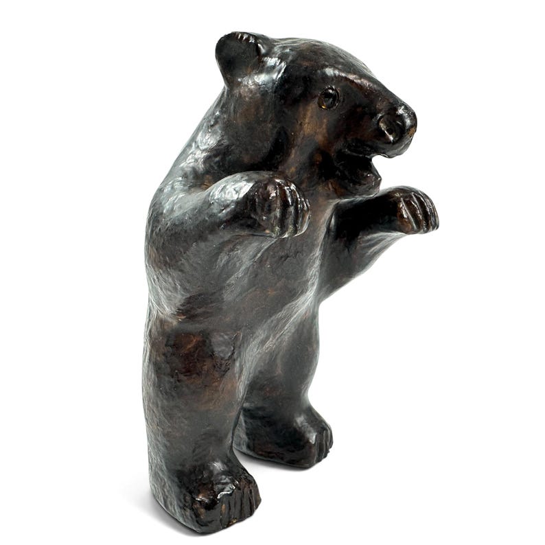 May include: A dark brown bear figurine standing on its hind legs with its front paws raised. The sculpture features a textured, glossy surface with visible brushstrokes and a slightly open mouth, capturing the animal in an upright, alert posture.
