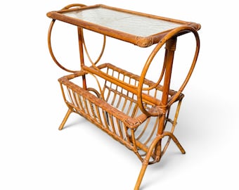 May include: A brown rattan side table featuring a rectangular top with a glass insert and a lower magazine rack. The structure is supported by four legs and includes two large circular side accents made of bent rattan poles.