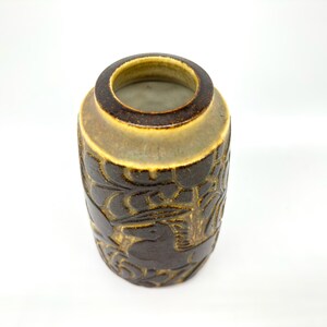 Peut inclure: Un vase en c&eacute;ramique marron avec un motif sculpt&eacute; textur&eacute;. Le vase a une forme cylindrique avec une large ouverture et un bord marron clair contrastant. Le motif sculpt&eacute; pr&eacute;sente un motif floral ou de feuilles r&eacute;p&eacute;titif.