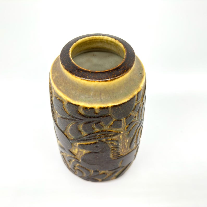 Peut inclure: Un vase en c&eacute;ramique marron avec un motif sculpt&eacute; textur&eacute;. Le vase a une forme cylindrique avec une large ouverture et un bord marron clair contrastant. Le motif sculpt&eacute; pr&eacute;sente un motif floral ou de feuilles r&eacute;p&eacute;titif.
