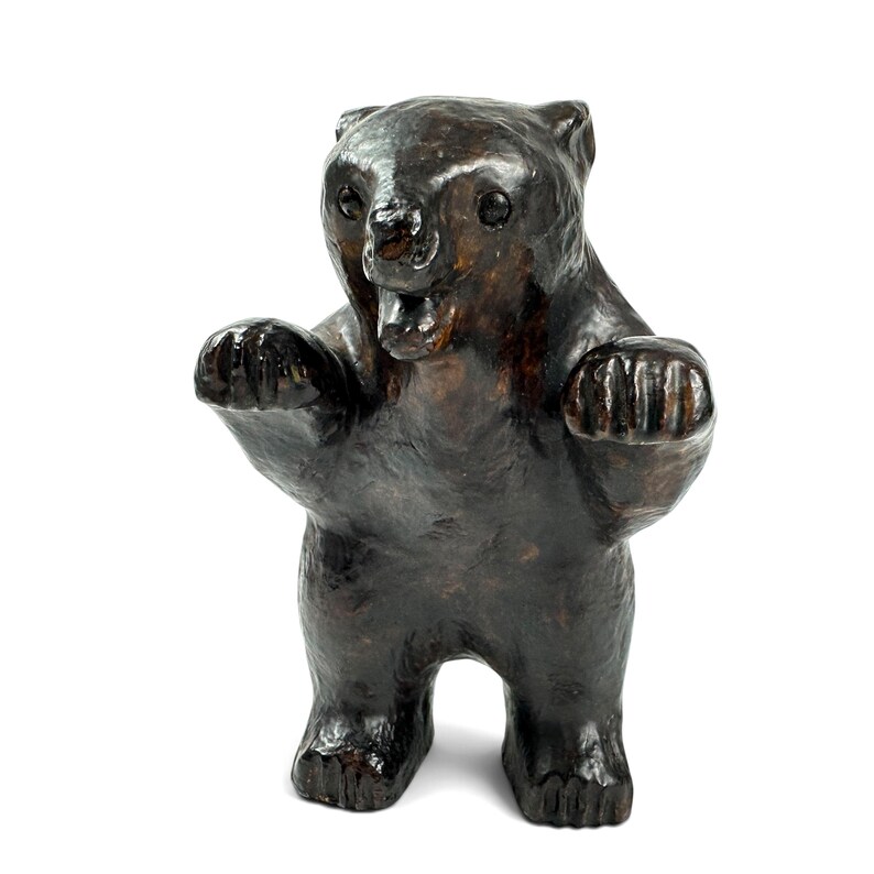 May include: A dark brown bear figurine standing on its hind legs with front paws raised. The bear has a glossy, textured surface, visible ears, a slightly open mouth, and carved details on its paws, presented against a plain white background.