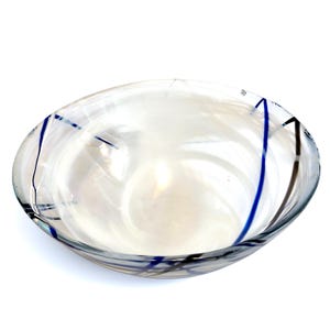 Pu&ograve; includere: Una ciotola in vetro trasparente caratterizzata da una finitura bianca iridescente a vortice su tutto l'interno. L'esterno &egrave; decorato con sottili linee incrociate blu scuro e nere, che creano un motivo geometrico sulla superficie curva.