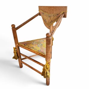 May include: A wooden chair featuring a carved rectangular backrest, a triangular seat, and armrests. The chair includes a triangular back cushion and a triangular seat cushion, both decorated with a moth pattern in yellow and brown, finished with yellow tassels.