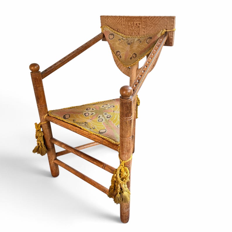 May include: A wooden chair featuring a carved rectangular backrest, a triangular seat, and armrests. The chair includes a triangular back cushion and a triangular seat cushion, both decorated with a moth pattern in yellow and brown, finished with yellow tassels.