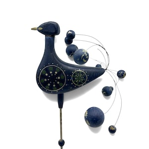 May include: A dark blue wooden bird garden stake featuring a painted green and white circular pattern on its body. The bird has a gold-colored beak and a decorative tail made of thin metal wires tipped with small, round, dark blue wooden spheres.