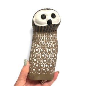 K&ouml;nnte beinhalten: Eine Eulenfigur aus Keramik mit einem glatten wei&szlig;en Gesicht, gro&szlig;en schwarzen Augen und einem schwarzen Schnabel. Der K&ouml;rper ist mattbraun und mit wei&szlig;en Mustern bemalt, darunter ein Gitterdesign auf der Brust und kreisf&ouml;rmige Federmotive.