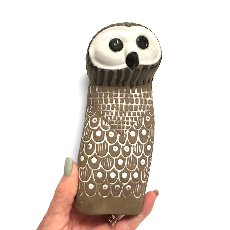 K&ouml;nnte beinhalten: Eine Eulenfigur aus Keramik mit einem glatten wei&szlig;en Gesicht, gro&szlig;en schwarzen Augen und einem schwarzen Schnabel. Der K&ouml;rper ist mattbraun und mit wei&szlig;en Mustern bemalt, darunter ein Gitterdesign auf der Brust und kreisf&ouml;rmige Federmotive.