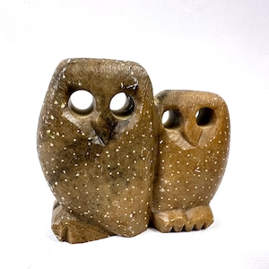 Op de afbeelding: Een bruine stenen uil sculptuur met twee uilen naast elkaar. De uilen hebben grote, ronde oogopeningen en zijn bespikkeld met witte stippen. De sculptuur is een decoratief item.