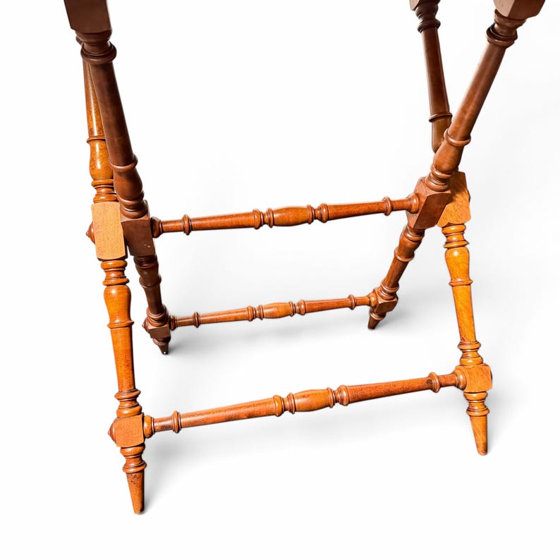 Puede incluir: Un soporte plegable de madera con cuatro patas torneadas en un acabado marr&oacute;n c&aacute;lido. La estructura incluye dos travesa&ntilde;os horizontales con detalles de husillo decorativos que conectan las patas para dar estabilidad al marco.
