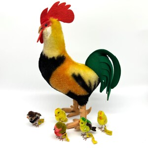 May include: A large, colorful rooster plush toy with a red comb and green tail, surrounded by several small chick plush toys. The rooster has yellow, orange, and black feathers. The chicks are yellow, brown, and green.