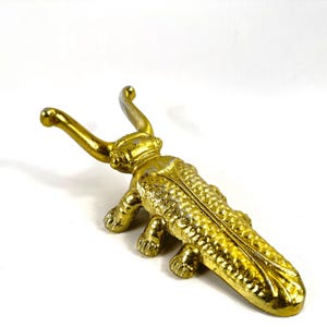 Może przedstawiać: Zestaw trzech ceramicznych kubków z nakrapianym, matowym wykończeniem. Kubki są w odcieniach kremu, jasnoszarości i ciemnoszarości. Każdy kubek ma prosty, minimalistyczny design, idealny do kawy lub herbaty.