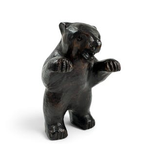 May include: A dark brown bear figurine standing on its hind legs with its front paws raised. The bear has a textured surface, visible ears, and an open mouth showing teeth. The sculpture is rendered in a deep, glossy brown finish throughout.