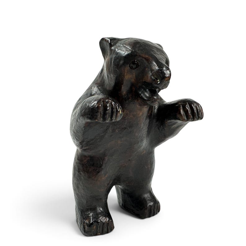 May include: A dark brown bear figurine standing on its hind legs with its front paws raised. The bear has a textured surface, visible ears, and an open mouth showing teeth. The sculpture is rendered in a deep, glossy brown finish throughout.