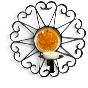 Peut inclure: Un bougeoir mural en m&eacute;tal noir compos&eacute; d'un cadre circulaire avec des volutes d&eacute;coratives et un disque en verre ambr&eacute; au centre. Une petite bougie chauffe-plat blanche est plac&eacute;e dans la coupelle en m&eacute;tal fix&eacute;e au bas du cadre.