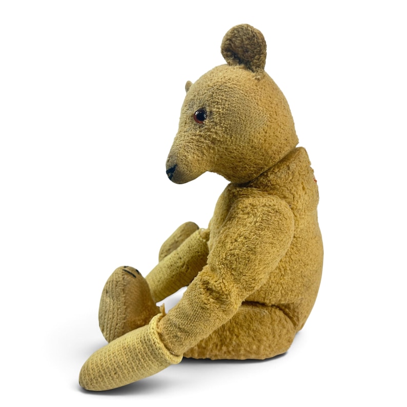 Pode incluir: Um urso de peluche de estilo vintage feito de tecido de pel&uacute;cia texturizado em tom castanho-dourado. O urso &eacute; apresentado numa posi&ccedil;&atilde;o sentada de perfil, com um nariz cosido em castanho escuro, pequenas orelhas redondas e olhos escuros brilhantes.