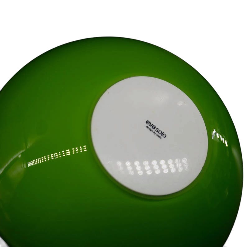 May include: A bright green bowl with a smooth, glossy finish. The underside features a circular white base centered on the bottom, which displays the black printed text "eva solo" followed by the smaller text "design by tools" underneath.