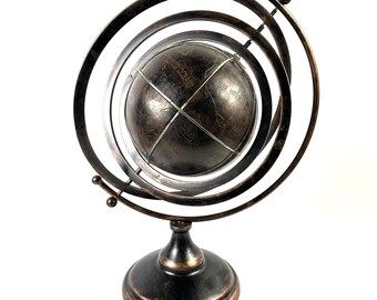 May include: A decorative globe with a dark bronze finish. The globe is encased in a series of metal rings and sits on a round base. The globe features visible continents and oceans, and is a decorative item.