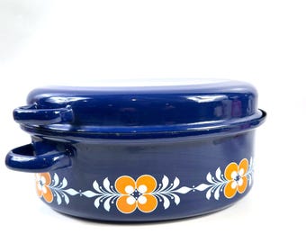 May include: A deep, oval-shaped blue enamel roasting pan with a matching lid. The exterior features a repeating decorative pattern of orange and white stylized flowers with leafy vines encircling the base. It includes two side handles.